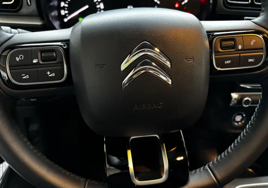 Gros plan sur le volant multifonctions noir avec logo chromé Citroën et commandes intégrées du tableau de bord C3 2024.