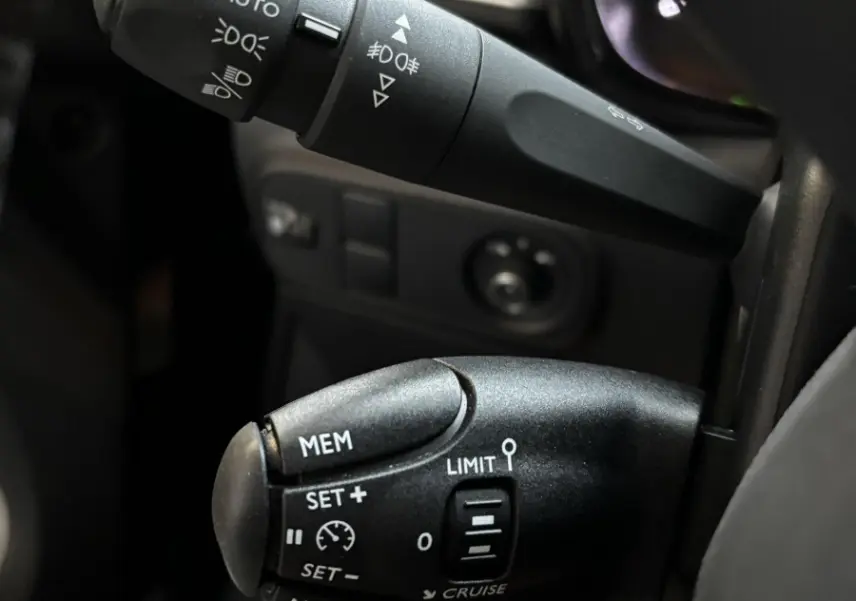 Gros plan sur les commandes au volant noir de la Citroën C3 2024, mettant en valeur les réglages des phares et du régulateur de vitesse.