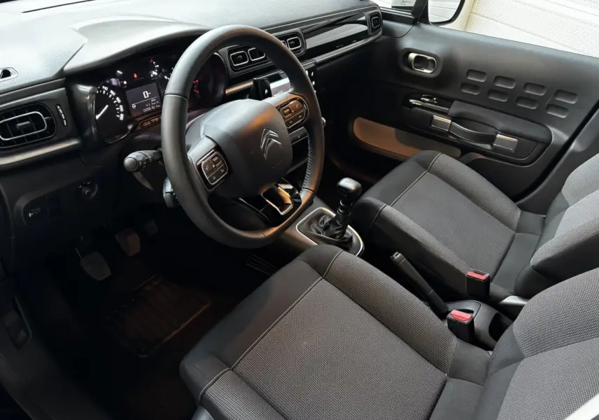 Vue intérieure côté conducteur de la Citroën C3 gris clair 2024 avec tableau de bord moderne et boîte manuelle.