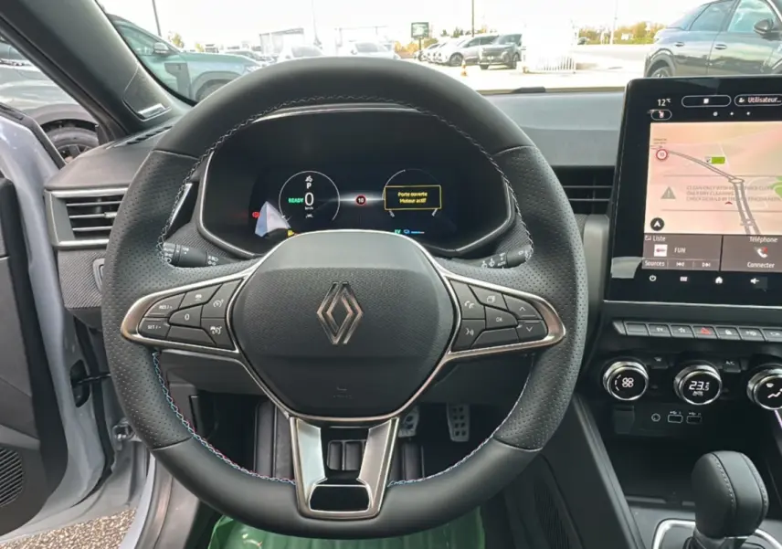 Vue intérieure centrée sur le volant cuir multifonctions d’une Renault Clio gris rafale avec écran tactile et tableau de bord numérique.