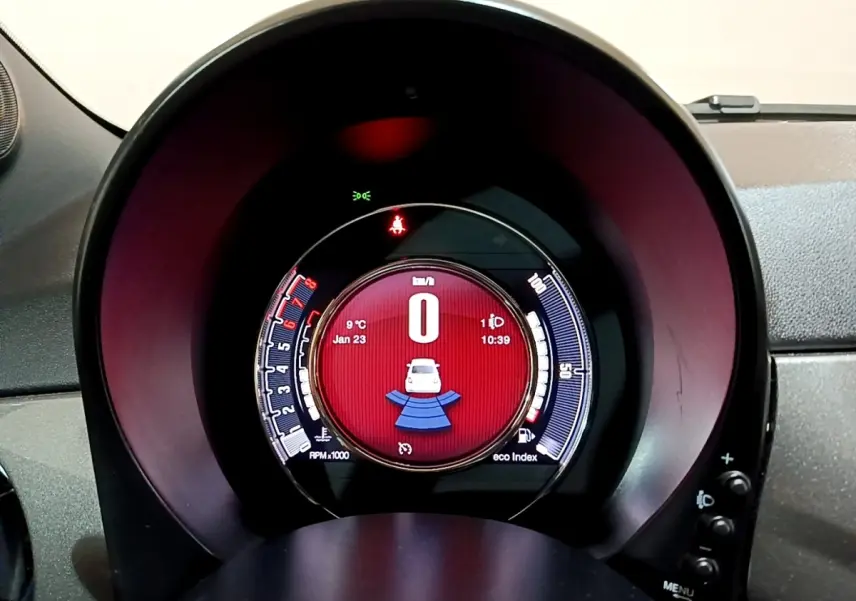 Gros plan sur le tableau de bord numérique circulaire de la Fiat 500 Hybrid avec affichage rouge et indicateurs blancs.