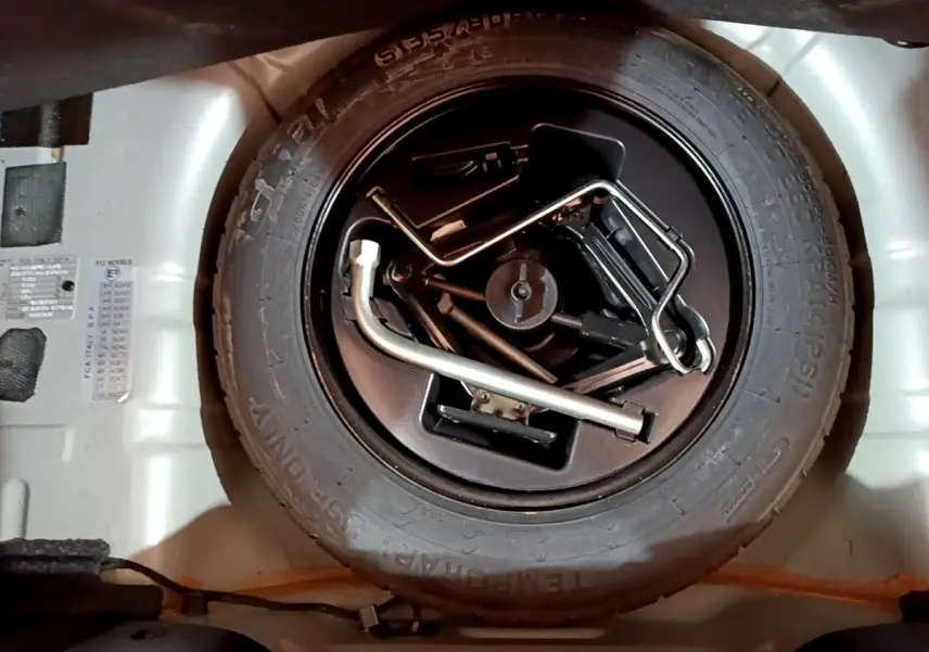 Gros plan sur la roue de secours et les outils de bord dans le coffre d'une FIAT 500 gris foncé.