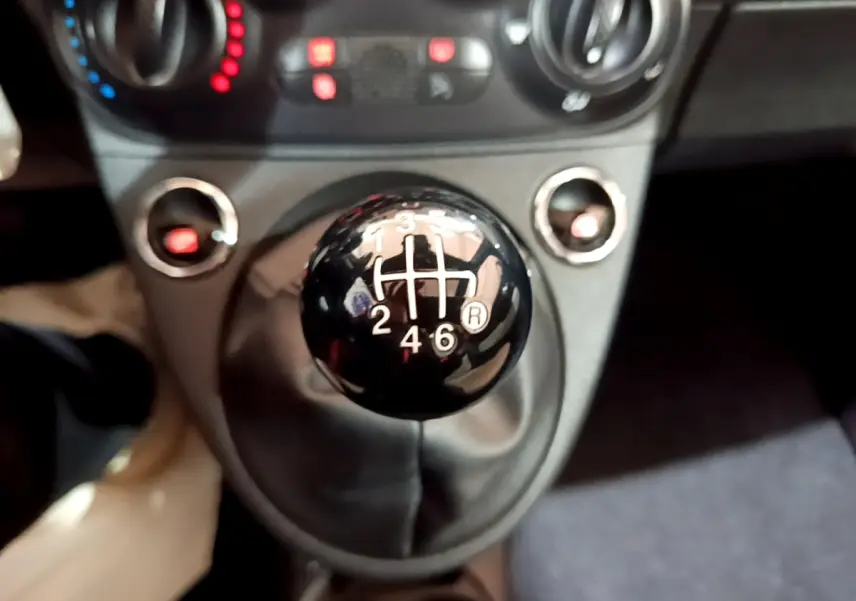 Gros plan sur le levier de vitesse manuel noir de la FIAT 500 Hybrid, avec tableau de bord et commandes en arrière-plan flou.
