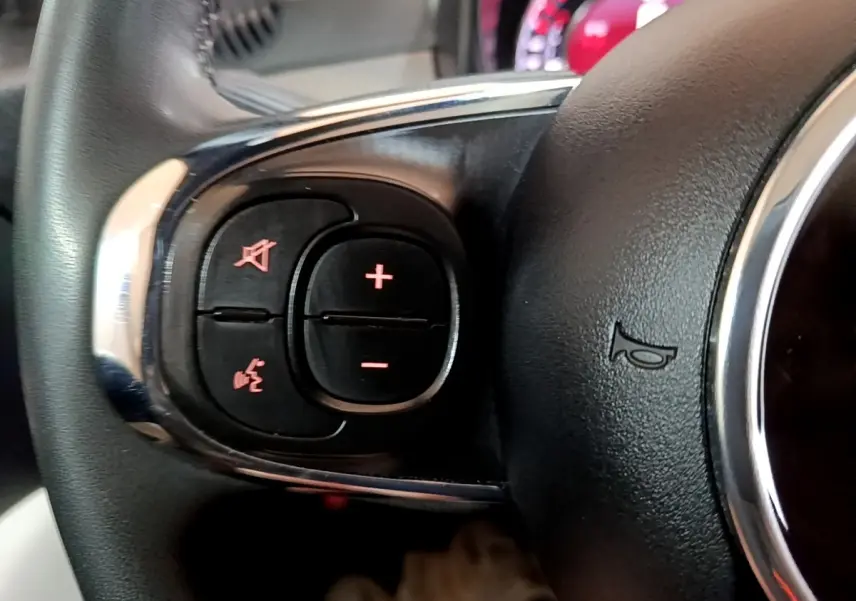 Gros plan sur le volant cuir noir multifonctions du Fiat 500 Hybrid, avec commandes de volume et téléphone intégrées.