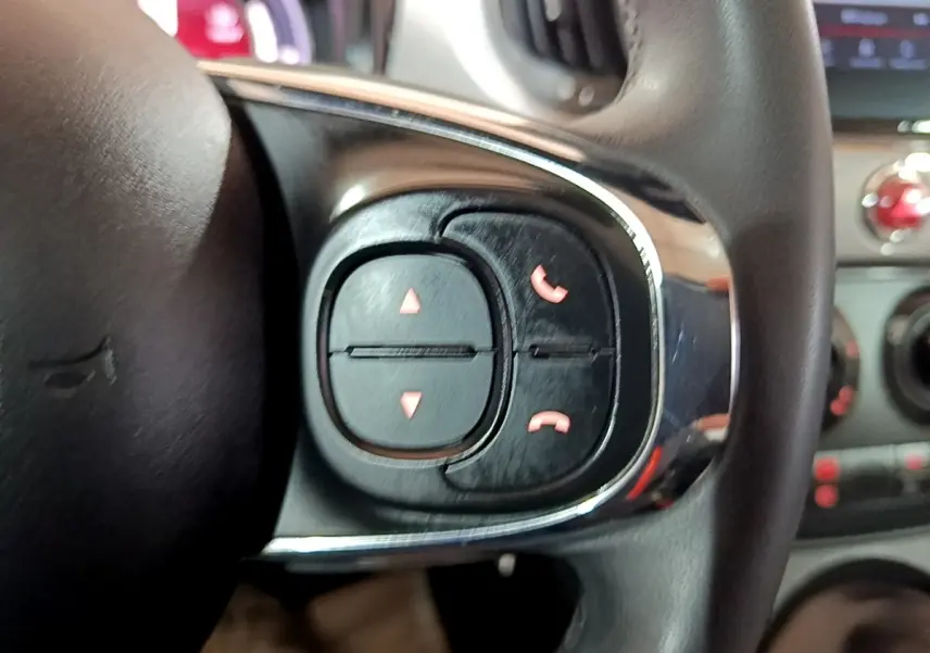 Gros plan sur les commandes du volant cuir noir de la Fiat 500 Hybrid, boutons de gestion d’appels visibles.