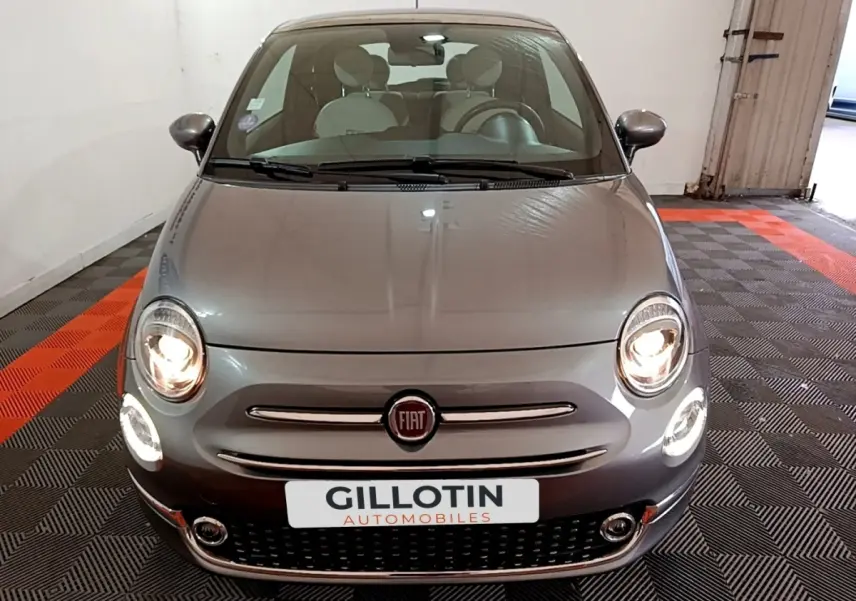 Vue avant d'une Fiat 500 gris foncé avec phares allumés dans un garage fermé.