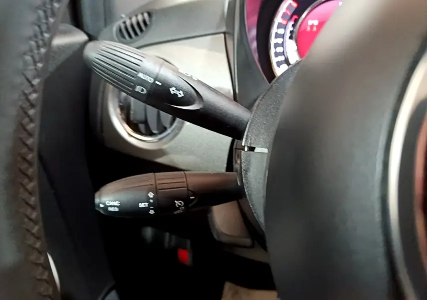 Gros plan sur les commandes au volant cuir de la FIAT 500 Hybrid gris foncé, avec tableau de bord partiellement visible.