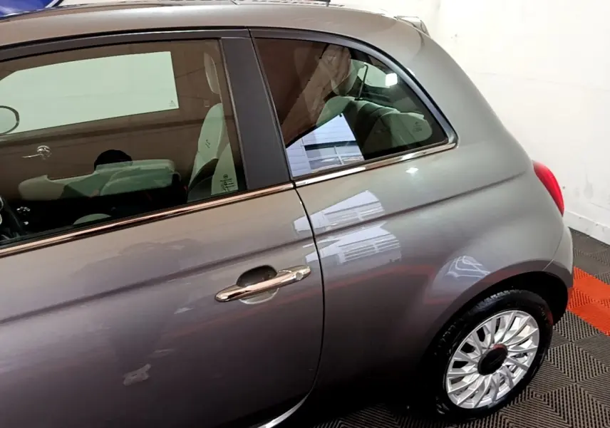 Vue côté gauche arrière d'une FIAT 500 Dolcevita hybride gris foncé avec jante argentée et poignée chromée.