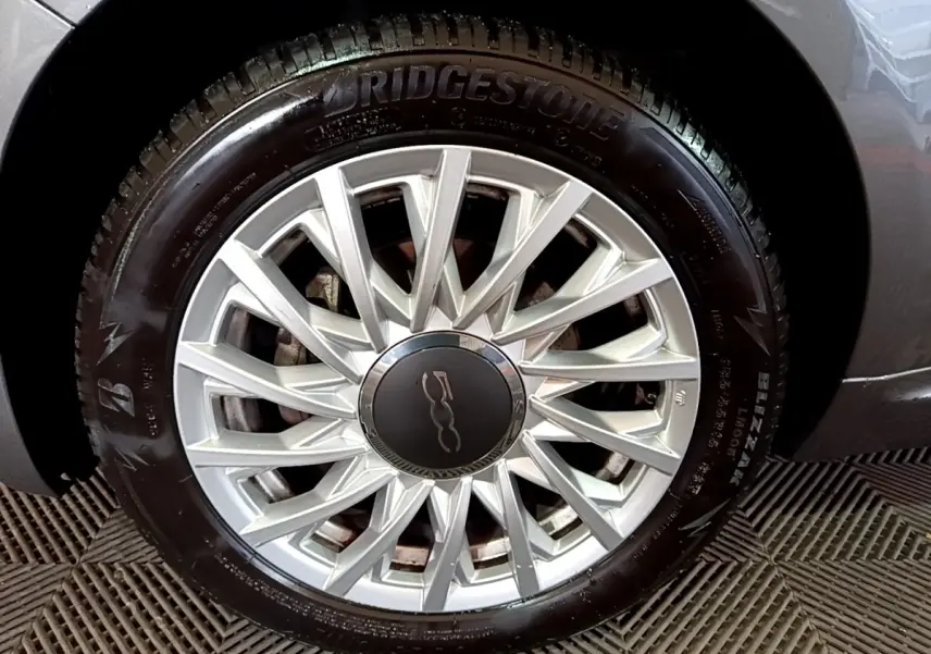 Gros plan sur la jante argentée et le pneu Bridgestone d'une FIAT 500 gris foncé, détail de la roue avant droite.