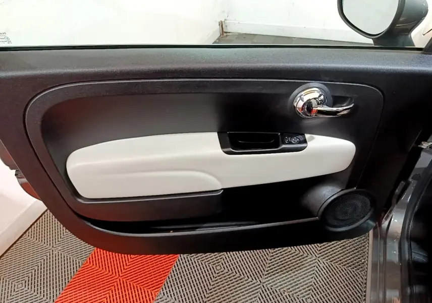 Vue intérieure du panneau de porte côté gauche de la Fiat 500 gris foncé avec poignée chrome et accoudoir clair.