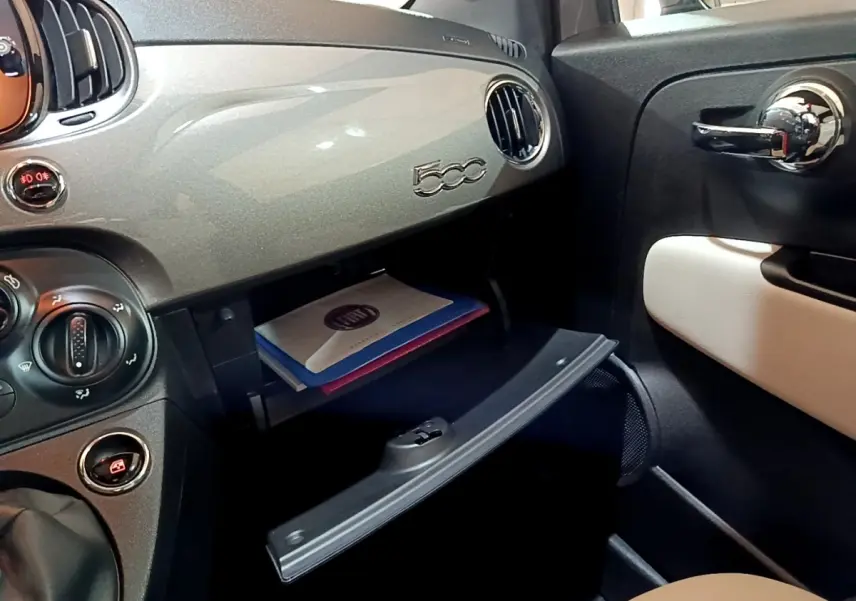 Vue intérieure côté passager du tableau de bord gris foncé de la FIAT 500 avec boîte à gants ouverte et porte chromée.