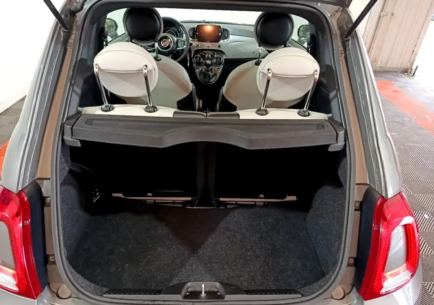 Vue arrière ouverte sur coffre et intérieur clair d'une Fiat 500 gris foncé avec tableau de bord et volant visibles.