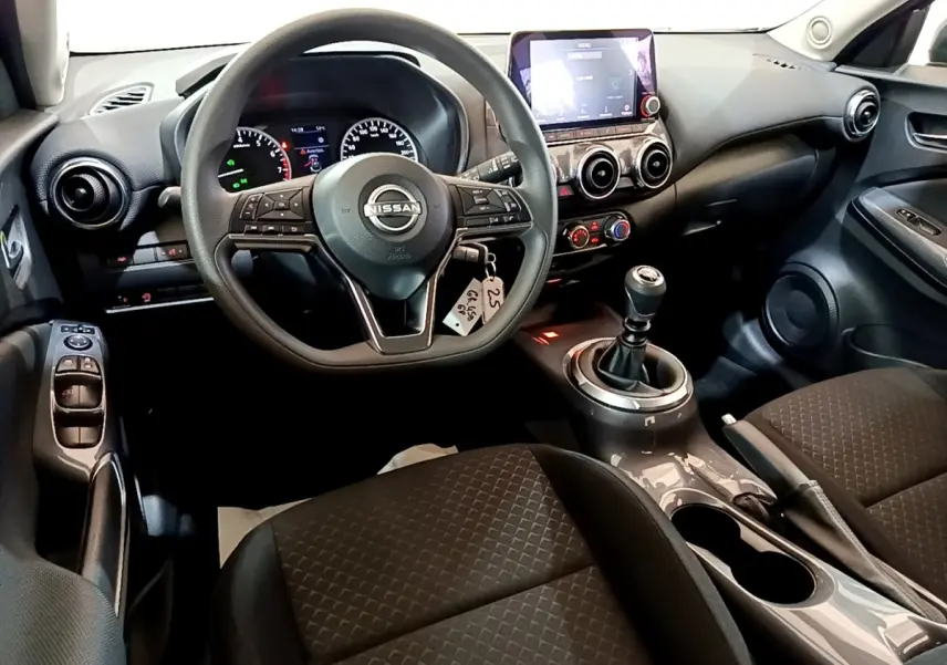 Vue intérieure avant du Nissan Juke noir 2023, volant multifonctions, écran tactile et levier de vitesse manuel visibles.