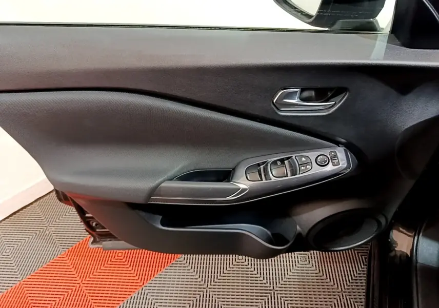 Vue intérieure côté gauche de la porte avant noire du Nissan Juke 2023, avec commandes électriques des vitres et rétroviseur.