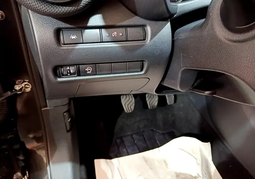 Vue intérieure côté conducteur du tableau de bord noir avec commandes d'assistance et pédales du Nissan Juke 2023.