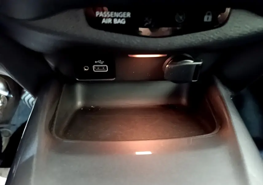 Gros plan sur la console centrale noire du Nissan Juke 2023 avec prise USB et allume-cigare éclairés.