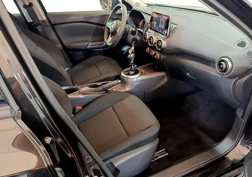 Vue intérieure côté conducteur du Nissan Juke noir 2023, montrant sièges, volant multifonctions et écran tactile central.