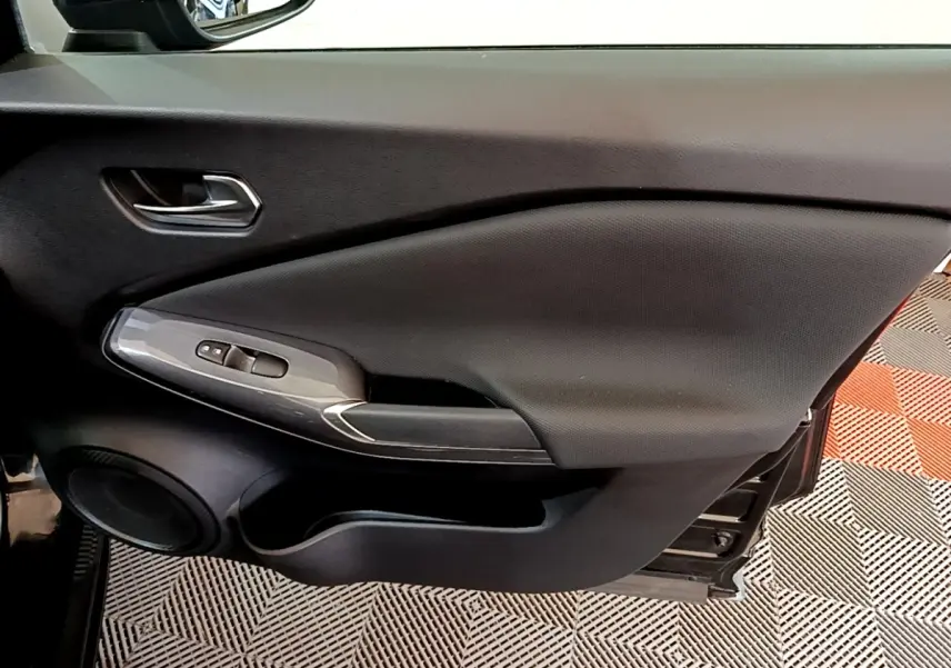 Vue intérieure du panneau de porte côté conducteur noir du Nissan Juke 2023 avec commandes de vitres et haut-parleur intégré.