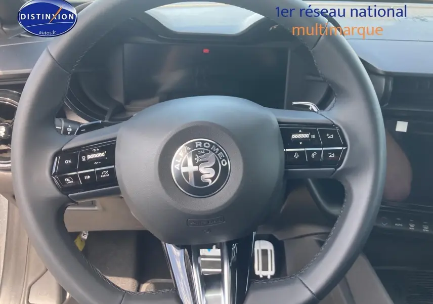 Vue rapprochée du volant noir de l'Alfa Romeo Junior 1.2 hybride avec commandes intégrées et tableau de bord digital.