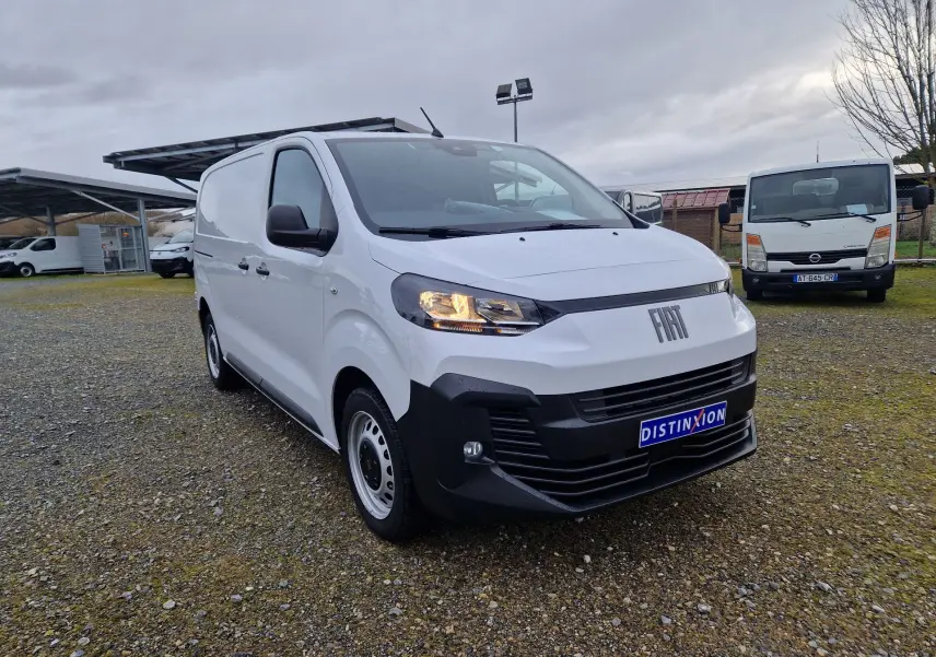 Fiat Scudo Fourgon blanc en 3/4 avant droit, avec calandre noire et plaque de protection, sur parking extérieur.