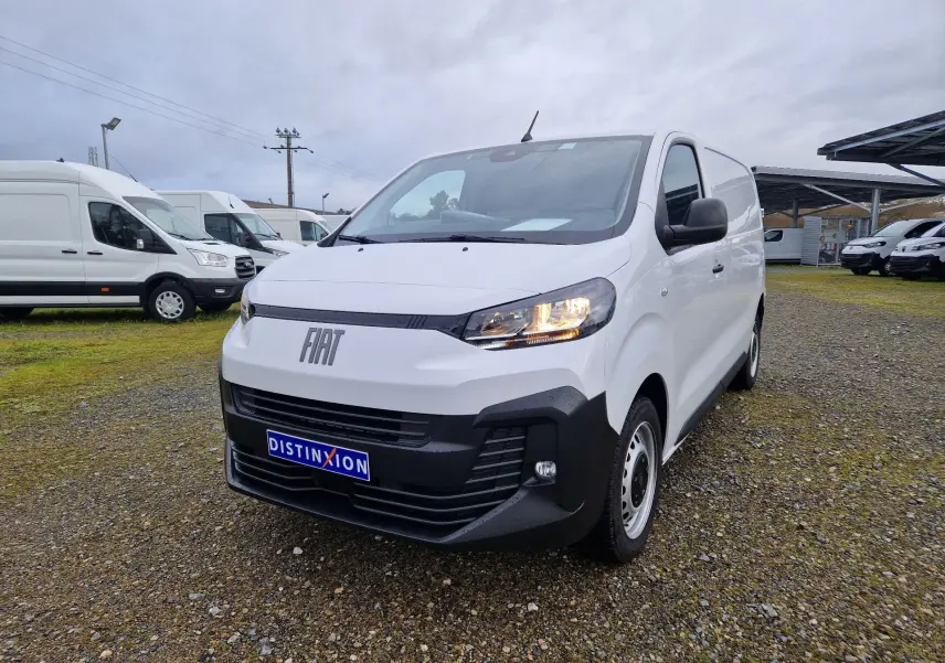 Fiat Scudo Fourgon blanc en 3/4 avant droit, avec calandre noire et phares allumés sur terrain extérieur.