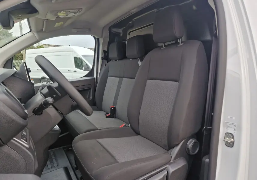 Vue intérieure côté conducteur du FIAT Scudo Fourgon blanc 2024, montrant les sièges tissu gris et noir, avec tableau de bord partiel.