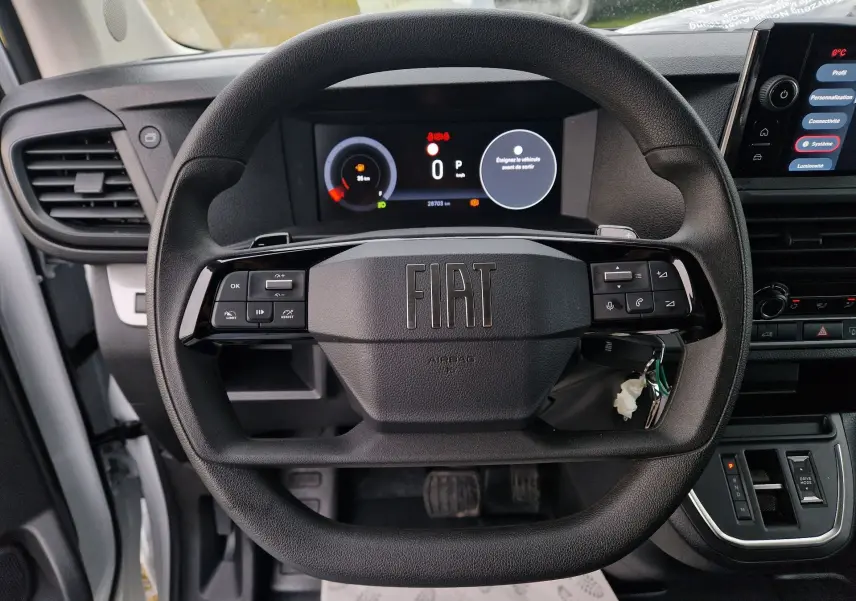 Vue intérieure centrée sur le volant noir du Fiat Scudo Fourgon 2024 avec tableau de bord numérique et console centrale visible.