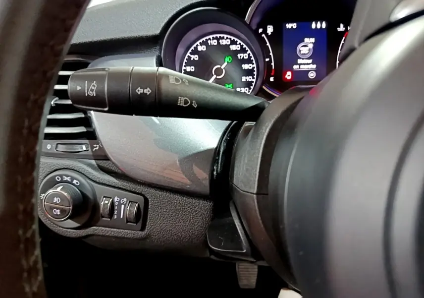 Gros plan sur le combiné d'instruments et commandes de phares à gauche du volant d'une FIAT 500X gris foncé, 2019.