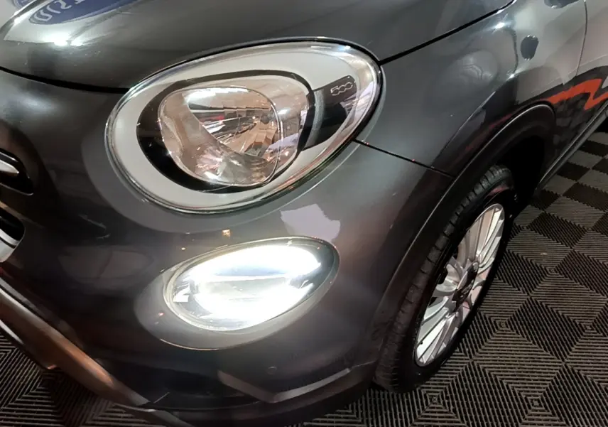 Gros plan sur l'avant droit gris foncé du FIAT 500X 2019, mettant en valeur le phare et le feu antibrouillard allumé.