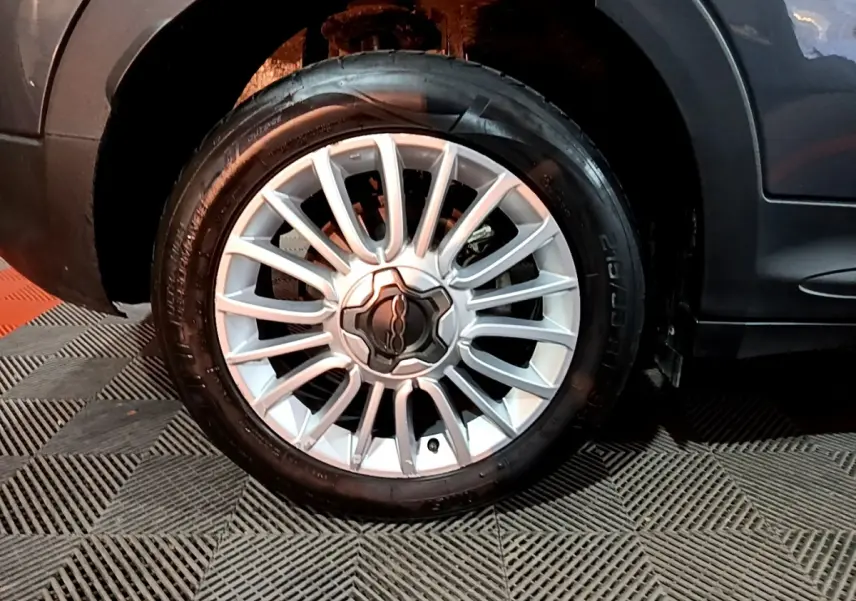 Gros plan sur la roue avant droite avec jante argentée du FIAT 500X gris foncé, partie basse de la carrosserie visible.