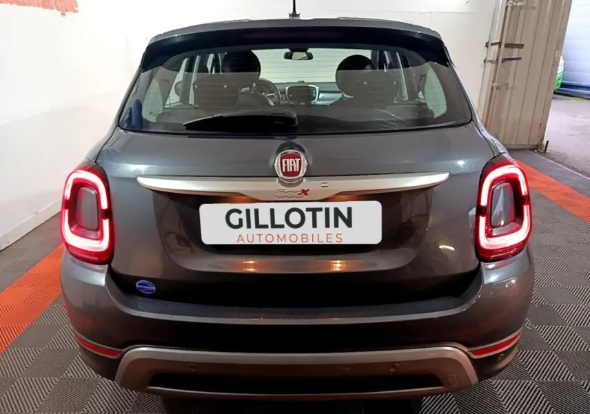Vue arrière d'une FIAT 500X gris foncé avec feux arrière allumés et logo FIAT visible sur le hayon.