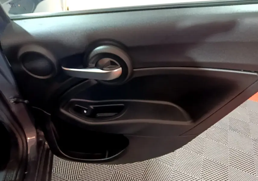 Vue rapprochée de la porte intérieure côté gauche gris foncé du FIAT 500X 2019 avec poignée argentée et commande de vitre.