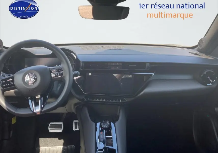 Vue intérieure frontale de l'Alfa Romeo Junior 1.2 hybride 2026 avec tableau de bord noir et écran tactile central.