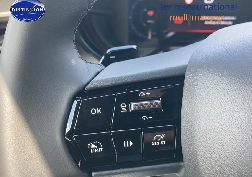 Gros plan sur les commandes au volant noir de l'Alfa Romeo Junior 1.2 hybride, mettant en valeur les boutons d'assistance et régulateur.
