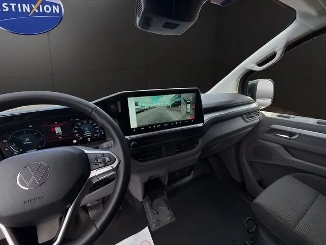 Vue intérieure côté conducteur du Volkswagen Transporter noir 2026, avec tableau de bord digital et grand écran tactile central.