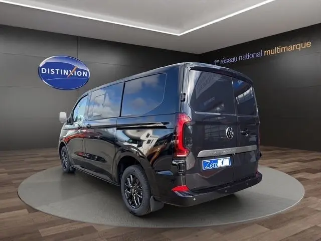 Vue 3/4 arrière droite d'un Volkswagen Transporter noir brillant avec feux arrière LED et jantes noires en showroom.