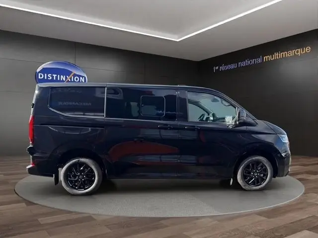 Vue latérale droite d’un Volkswagen Transporter noir 2026, avec jantes noires brillantes et vitres teintées, en showroom.