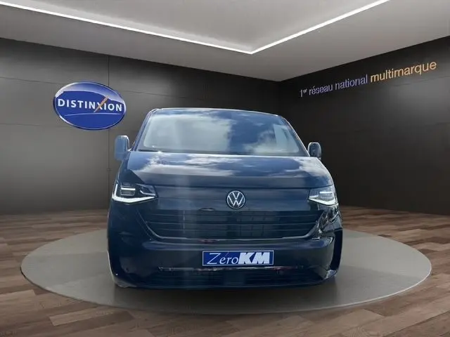 Vue de face d'un Volkswagen Transporter noir 2026 avec phares LED et calandre noire dans un showroom.