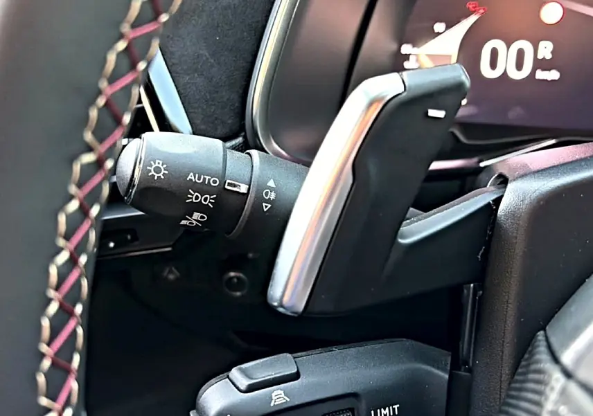 Détail du levier de vitesses automatique et commandes au volant en cuir noir avec surpiqûres rouges dans un DS7 noir.