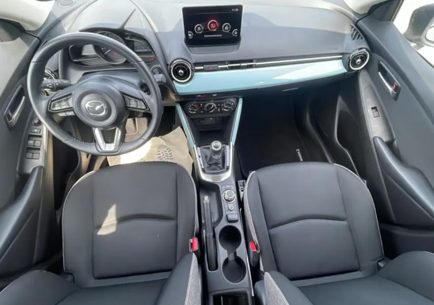 Vue intérieure avant de la Mazda2 2024, montrant tableau de bord, volant cuir multifonction et levier de vitesses manuel.
