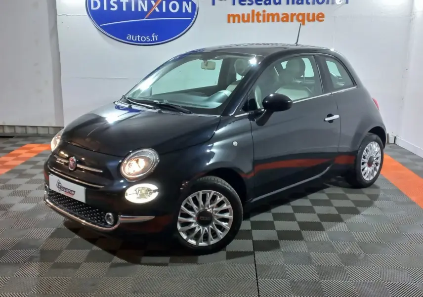 Vue 3/4 avant droite d'une Fiat 500 noire avec phares allumés dans un showroom intérieur.