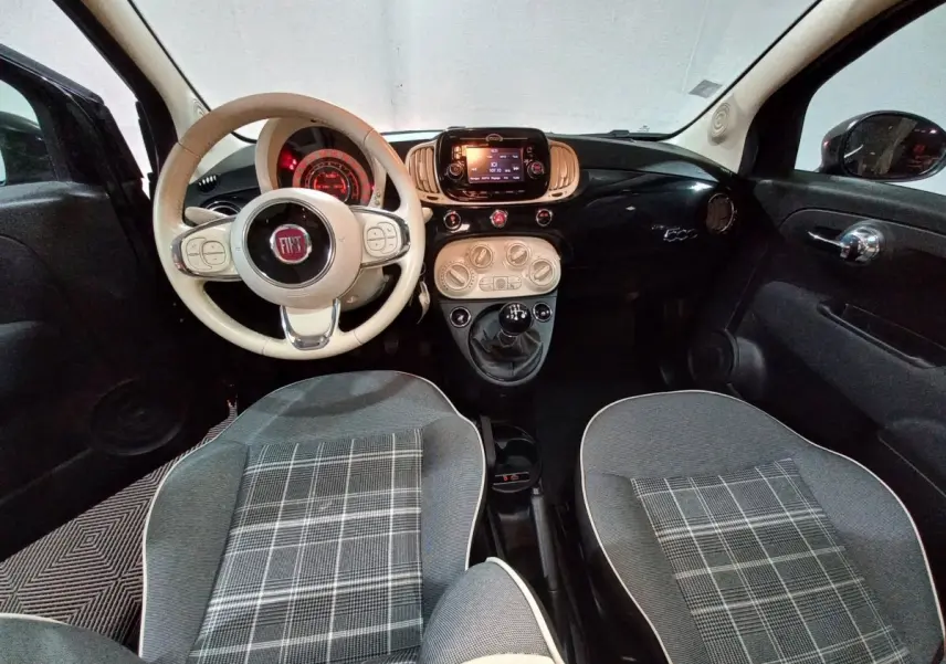Vue intérieure avant de la Fiat 500 noire, volant beige, tableau de bord noir brillant avec écran tactile central.