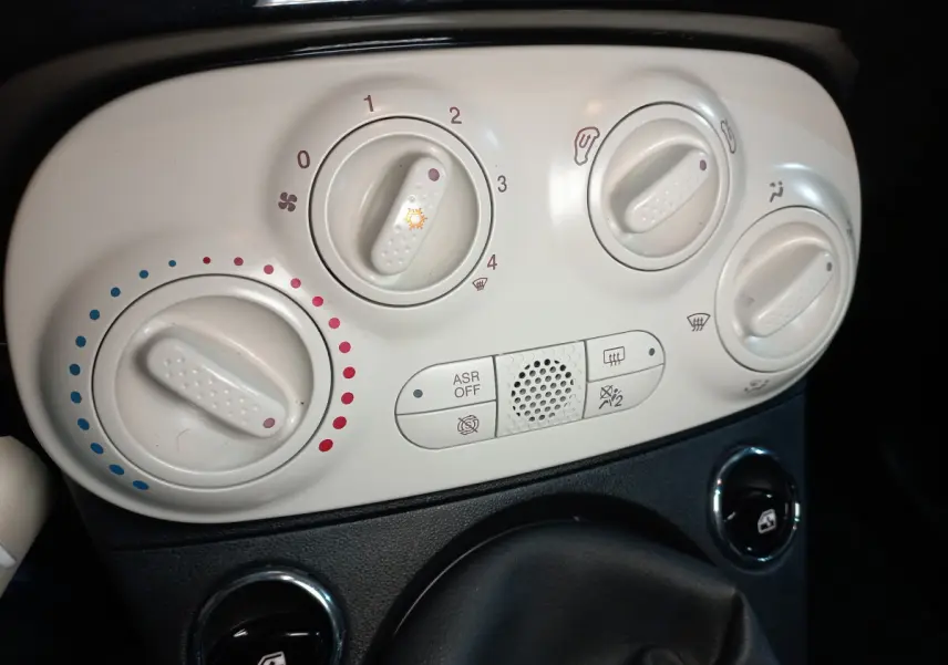 Gros plan sur les commandes de climatisation blanches du tableau de bord de la Fiat 500 noire, version Lounge 2018.