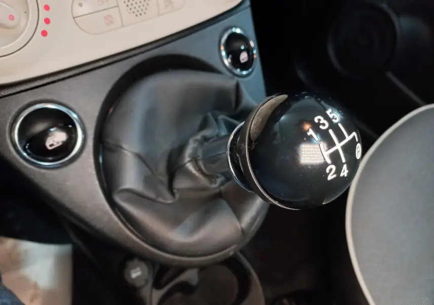 Gros plan sur le levier de vitesses manuel noir de la Fiat 500 Lounge, avec console centrale et sièges partiellement visibles.