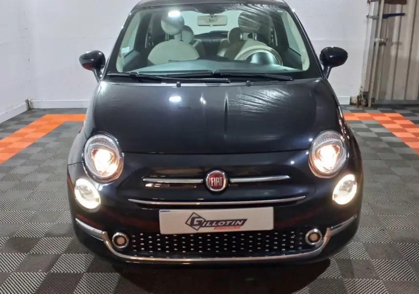 Vue de face d'une FIAT 500 noire avec phares allumés et intérieur clair visible au travers du pare-brise.