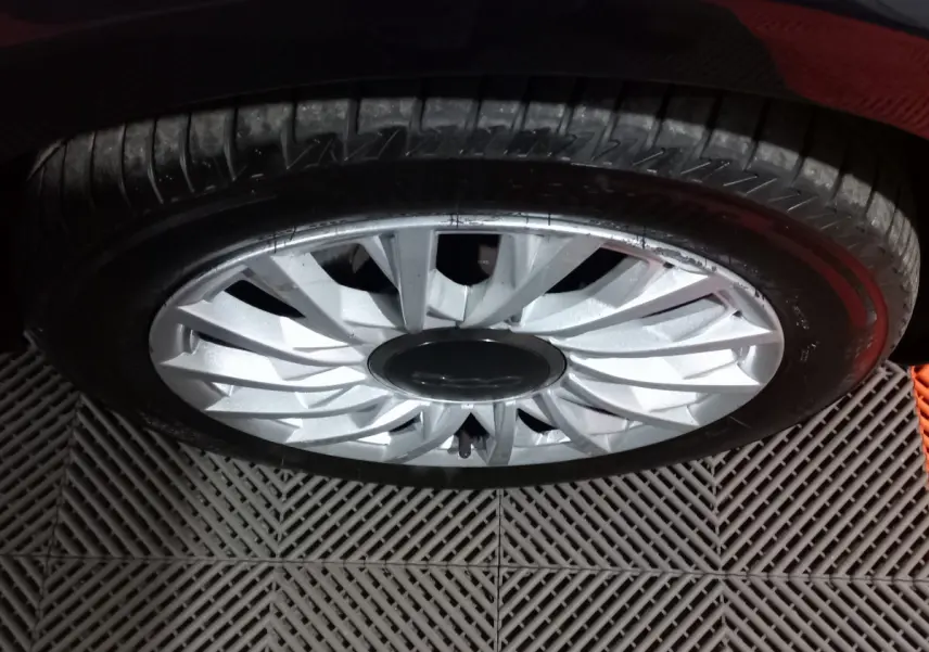 Gros plan sur la roue avant droite d'une FIAT 500 noire, mettant en valeur la jante argentée au design étoilé.