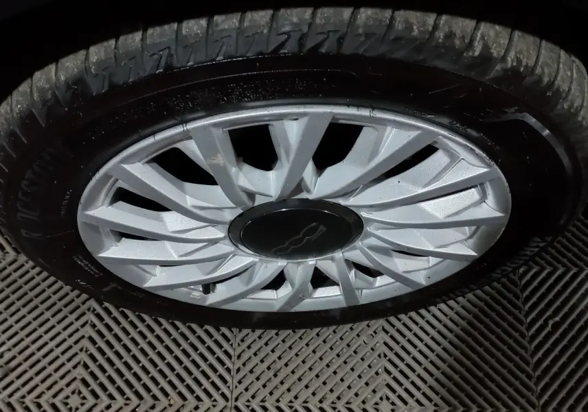 Gros plan sur la jante argentée d'une FIAT 500 noire, mettant en valeur le logo central distinctif.