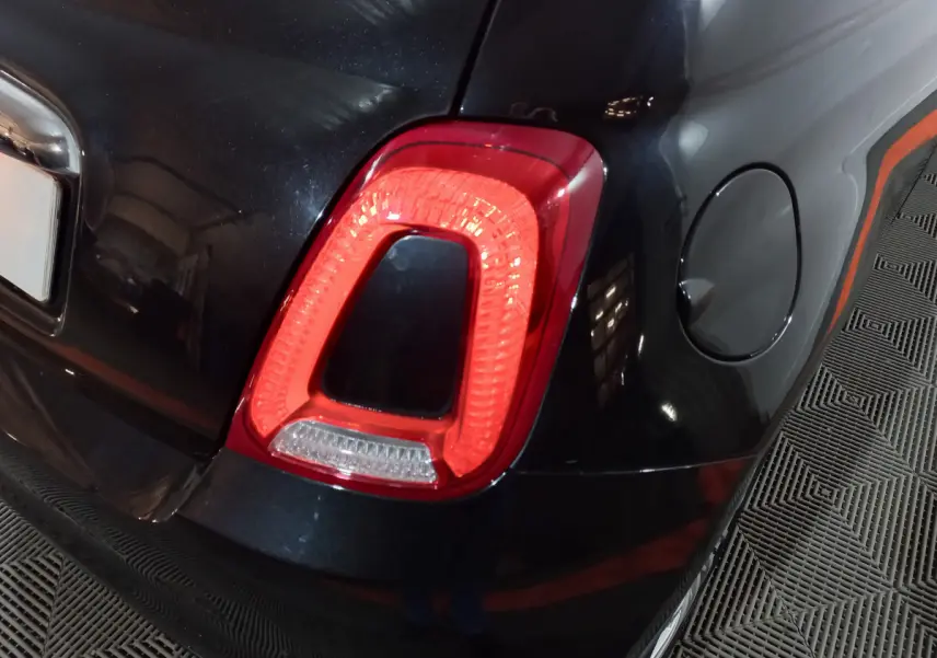 Gros plan sur le feu arrière droit rouge d'une FIAT 500 noire, avec trappe à carburant visible sur le côté droit.