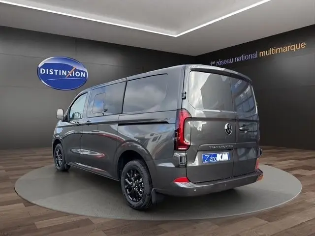 Vue 3/4 arrière droite d’un Volkswagen Transporter gris foncé avec jantes noires, présenté en showroom.