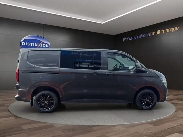 Vue de profil côté droit d’un Volkswagen Transporter gris foncé avec jantes noires en intérieur showroom.